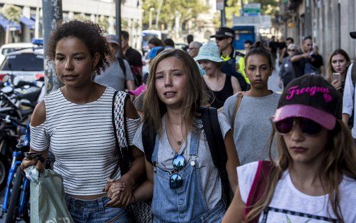 An woman accompanied by young people reacts after a van ploughed into the crowd, killing 13 persons and injuring several others on the Rambla in Barcelona on August 17, 2017. At least 13 people have been killed and dozens were injured after a white ...