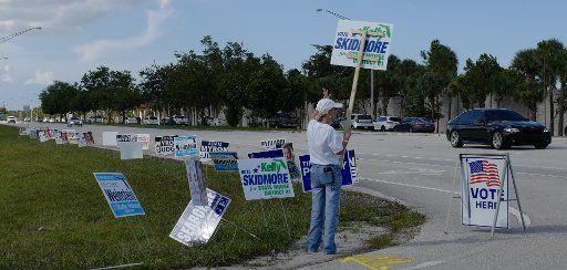 A candidate representative holds sign at the entrance to a polling station in Delray Beach, Florida on Tuesday, August 18,2020. Lines at the polling sites are shorter and in some cases nonexistent due to the COVID-19, Coronavirus Pandemic. Photo by Gary I Rothstein