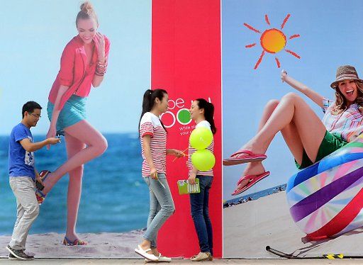 (130505) -- ZHENZHOU, May 5, 2013 (Xinhua) -- Young people wearing summer clothing walk past an advertisement board in Zhengzhou, capital of central China\