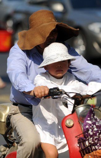 (130808) -- HANGZHOU, Aug. 8, 2013 (Xinhua) -- A citizen shields himself with his child from the scorching sun as riding on road in Hangzhou, capital of east China\