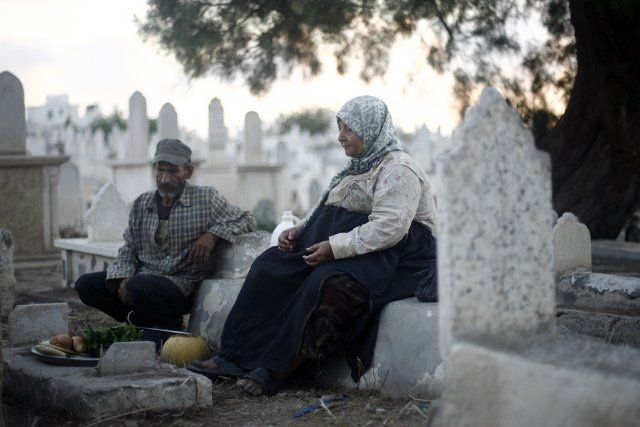 (130726) -- GAZA, July 26, 2013 (Xinhua) -- A Palestinian woman and her husband sit over a grave, waiting for breaking fast during the month of Ramadan, at a cemetery in Gaza City on July 26, 2013. The poor family have a small daily income, which ...