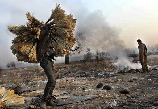 (131201) -- SRINAGAR, Dec. 1, 2013 (Xinhua) -- A non-Kashmiri worker carries brooms as another worker warms himself near a bonfire of garbage on a cold morning in Anantnag, some 60 kilometers south of Srinagar, summer capital of Indian-controlled ...