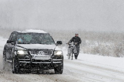 (131201) -- NARVA, Dec. 1, 2013 (Xinhua) -- A biker and a car moves forward on a street covered with snow in Narva, the third largest city with a population of about 60,000 in Northeast Estonia, Dec. 1, 2013. A snow storm hits Narva on Sunday, ...
