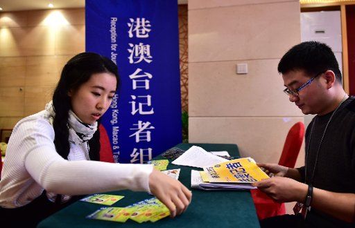 (160301) -- BEIJING, March 1, 2016 (Xinhua) -- A staff worker (R) hands out press card for a journalist of Hong Kong Wen Wei Po, who is here to cover the fourth annual session of the 12th National People\