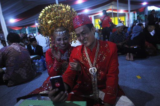 (180101) -- JAKARTA , Jan. 1, 2018 (Xinhua) -- A couple talk to their family on a smart phone before a mass wedding marking the new year of 2018 in Jakarta, Indonesia, on Dec. 31, 2017. (Xinhua\/Agung Kuncahya B.) (zf)