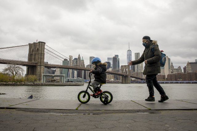 (200428) -- NEW YORK, April 28, 2020 (Xinhua) -- A senior walks with a child riding a bike in Main Street Park near the Brooklyn Bridge in New York, the United States, on April 27, 2020. As of Monday afternoon, the United States reported more than 980,000 COVID-19 cases with over 55,000 deaths, according to the Center for Systems Science and Engineering at Johns Hopkins University. (Photo by Michael Nagle\/Xinhua