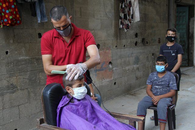 (200831) -- GAZA, Aug. 31, 2020 (Xinhua) -- A Palestinian barber wearing a mask and gloves shaves for a boy free of charge during the lockdown to curb the spread of COVID-19, in Gaza City, on Aug. 31, 2020. Palestine recorded the highest daily rise of COVID-19 cases on Monday after the outbreak of the deadly pandemic in the Palestinian territories in March. The health ministry recorded in the last 24 hours seven deaths and 875 new COVID-19 cases in the West Bank, East Jerusalem, and the Gaza Strip. (Photo by Rizek Abdeljawad\/Xinhua