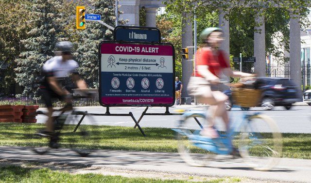 (210612) -- TORONTO, June 12, 2021 (Xinhua) -- Cyclists pass a billboard reminding people to practice physical distancing in Toronto, Canada, on June 12, 2021. Canada reported 1,115 new daily cases of COVID-19 on Saturday, bringing the cumulative total to 1,400,827, including 25,910 deaths, according to CTV. (Photo by Zou Zheng\/Xinhua