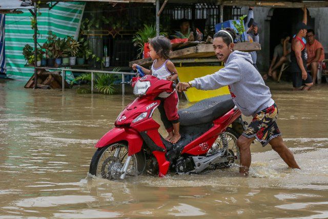 (220926) -- BULACAN, Sept. 26, 2022 (Xinhua) -- A man pushes his motorcycle with a child on board through a flooded road in Bulacan Province, the Philippines, Sept. 26, 2022. Super typhoon Noru slammed Luzon island in the Philippines with heavy rainfall and winds since Sunday afternoon, leaving five people dead, as it blew away from the Southeast Asian country on Monday. (Xinhua\/Rouelle Umali